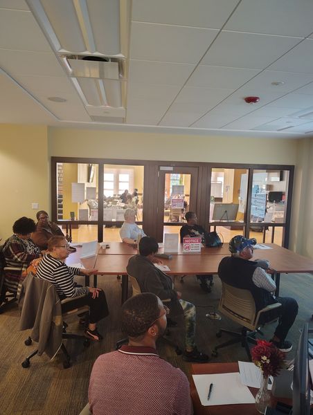 Photo of a computer class in Room 109 taught by instructor Diomaris Gomez, showing participants seated at tables during a lesson on confident internet browsing held on April 14 at 11 p.m., with desktop computers visible around the room.