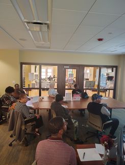 Photo of a computer class in Room 109 taught by instructor Diomaris Gomez, showing participants seated at tables during a lesson on confident internet browsing held on April 14 at 11 p.m., with desktop computers visible around the room.