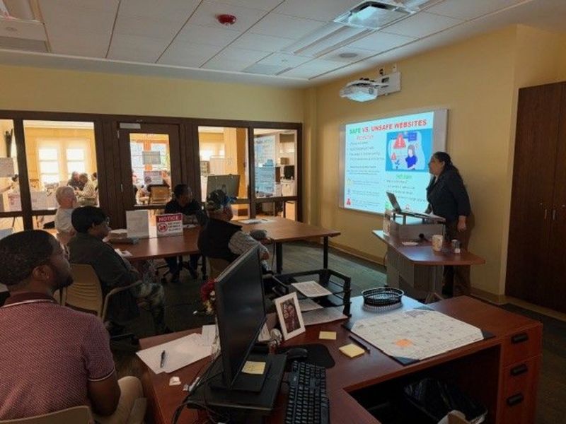 Photo of a computer class in Room 109 taught by instructor Diomaris Gomez, showing participants seated at tables during a lesson on confident internet browsing held on April 14 at 11 p.m., with desktop computers visible around the room.