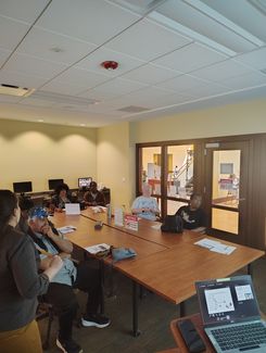 Photo of a computer class in Room 109 taught by instructor Diomaris Gomez, showing participants seated at tables during a lesson on confident internet browsing held on April 14 at 11 p.m., with desktop computers visible around the room.