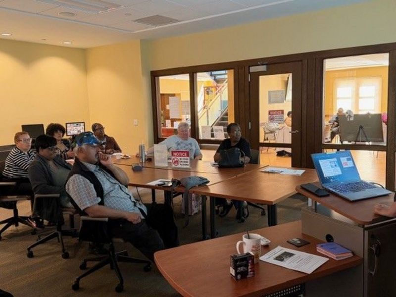 Photo of a computer class in Room 109 taught by instructor Diomaris Gomez, showing participants seated at tables during a lesson on confident internet browsing held on April 14 at 11 p.m., with desktop computers visible around the room.